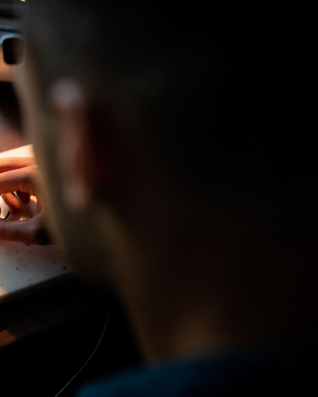 Engineer hand-soldering a small circuit board under a bench lamp.